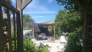 Un jardín con un pérgola de madera, plantas en macetas y un muro de piedra.