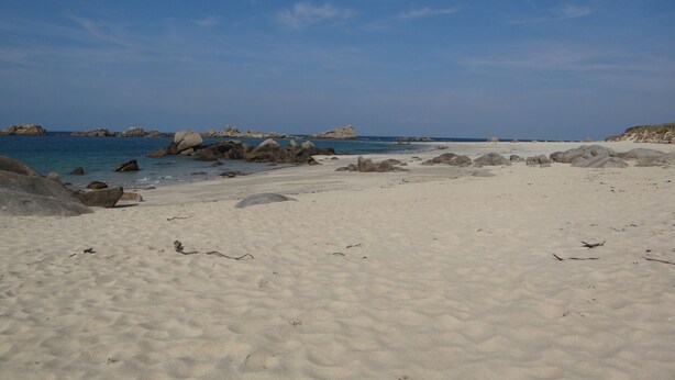 Una playa arenosa con rocas grandes y agua tranquila.