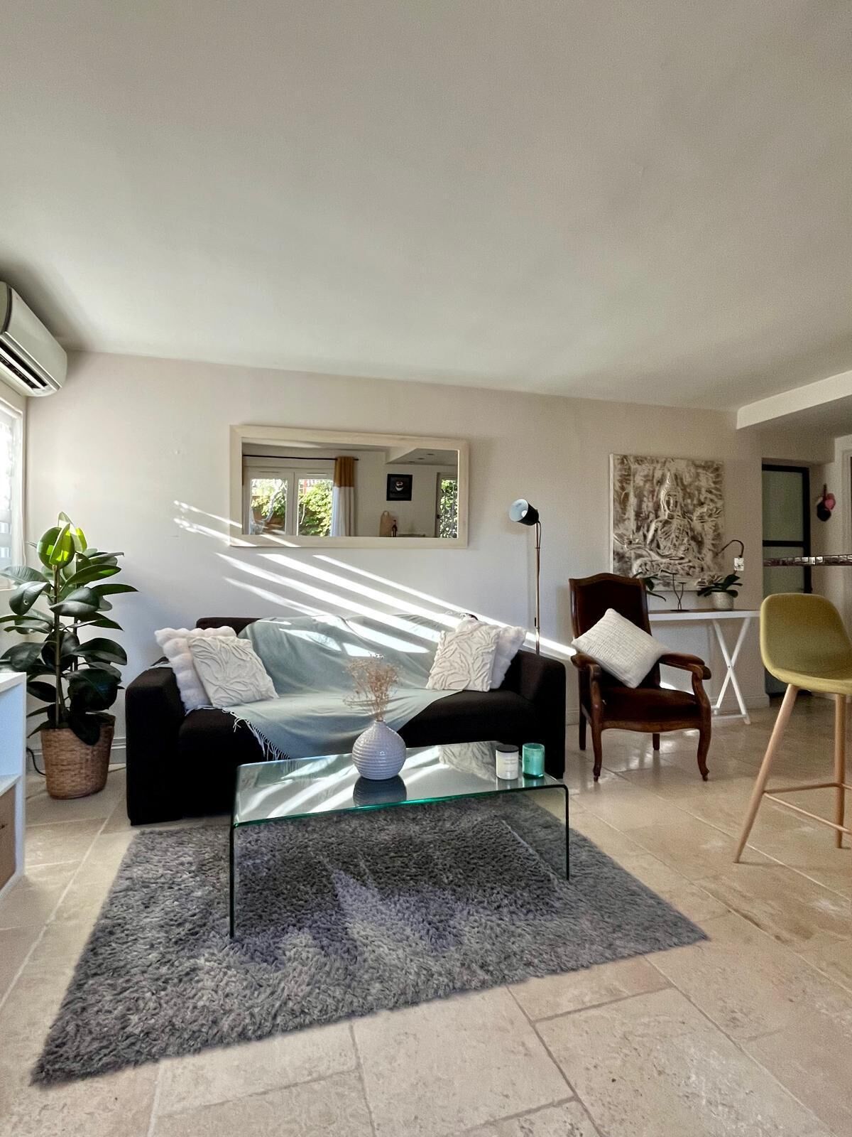A modern living room with a glass coffee table, a black sofa, a wooden chair, and a potted plant.