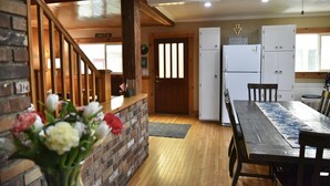 A cozy kitchen with wooden flooring, a dining table with chairs, a refrigerator, and a ceiling fan.