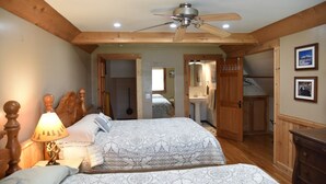 A bedroom with two beds, a ceiling fan, wooden beams, a lamp, and a dresser.
