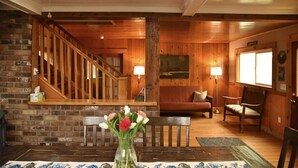 A wooden interior with a staircase, a sofa, and a dining table with a vase of flowers.