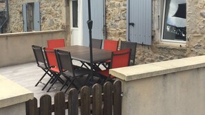 A stone building with a balcony, a table with chairs, and an umbrella.