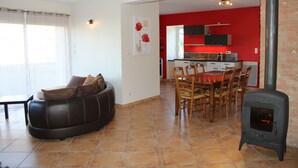 A living room with a sofa, dining table, chairs, and a wood-burning stove.
