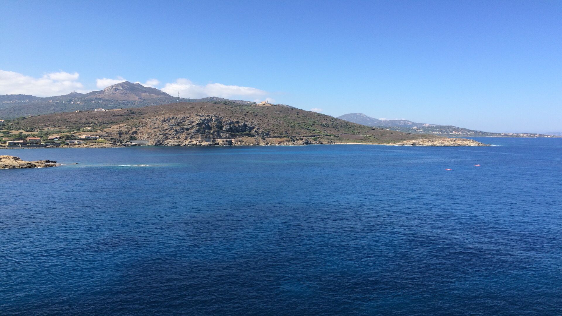 A coastal landscape with a clear view of the sea, rocky terrain, and distant hills.