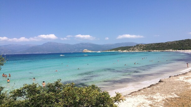 A beach with clear turquoise water, people swimming and sunbathing, and mountains in the background. - CASA VERDE - VILLA **** - Heated swimming pool - Near L'Ile-Rousse beach (Monticello)
