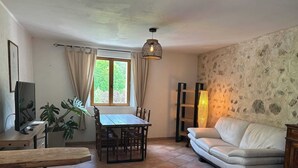 Een woonkamer met een eettafel, een witte bank en een televisie op een houten dressoir.