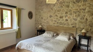 Een slaapkamer met een stenen muur, een houten bed, twee nachtkastjes met lampen, een raam met gordijnen, en een radiator.