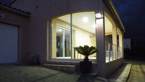 Una casa con un'ampia porta in vetro che dà su uno spazio interno, una pianta in vaso davanti e una scala che conduce a una zona coperta.