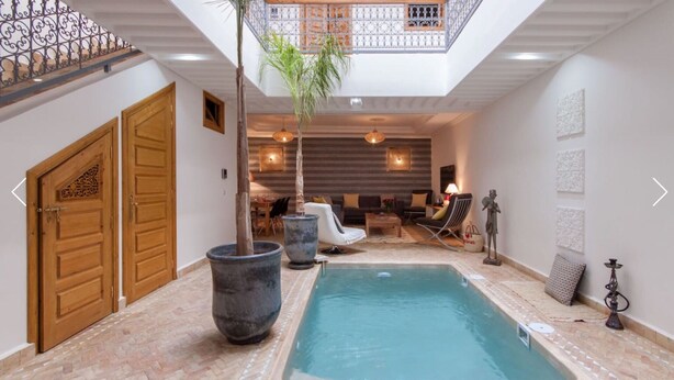 A pool area with a wooden door, a large planter, and a seating area with a sofa and chairs. - Riad Melilo heated swimming pool 2 steps from Jeema el Fna square (Marrakech)