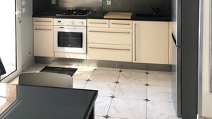 Une cuisine moderne équipée d’une cuisinière à gaz, d’un four, d’appareils électroménagers en acier inoxydable et d’un grand luminaire suspendu.