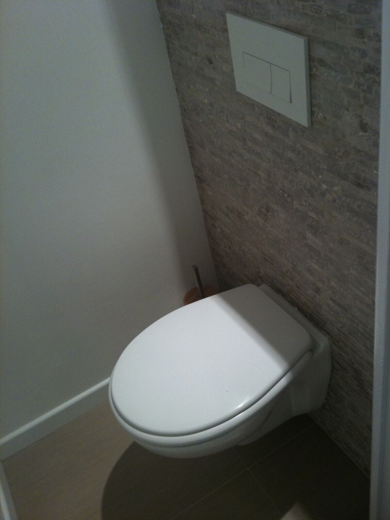 A small, white toilet in a bathroom with a stone wall and a white door.