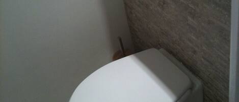 A small, white toilet in a bathroom with a stone wall and a white door.