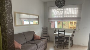 A living room with a grey sofa, a dining table with chairs, a window with sheer curtains, and a hanging light fixture. - MENTON, 2 STEPS FROM THE SEA, CITY CENTER, STUDIO 2 ROOMS, QUALITY BENEFITS (Menton)