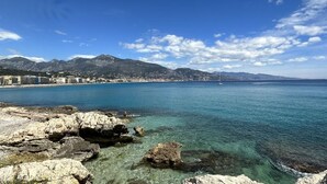 A coastal cityscape with clear blue waters, rocky shoreline, and mountains in the background. - MENTON, 2 STEPS FROM THE SEA, CITY CENTER, STUDIO 2 ROOMS, QUALITY BENEFITS (Menton)