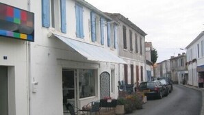 Una calle estrecha con coches aparcados y edificios con contraventanas azules.