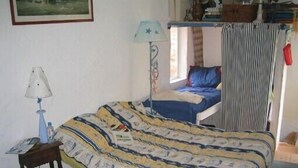 Un dormitorio con cama, mesita de noche, lámpara, ventana con cortinas y un cuadro en la pared.