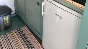 Une cuisine de taille réduite, équipée d’un évier, d’un petit réfrigérateur et d’un crédence carrelée.