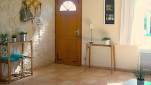 Una habitación con pared de piedra, puerta de madera, una pequeña mesa con lámpara y una planta en maceta.
