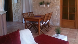 Un comedor con una mesa y sillas de madera, un muro de piedra, un reloj y una puerta con paneles de vidrio.