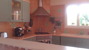Una cocina con armarios verdes, una estufa y una ventana con vistas a árboles.