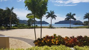 Una playa con palmeras, una zona arenosa y vistas al mar y a las montañas.