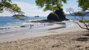 Una playa con agua cristalina, una gran formación rocosa y islas a la distancia.