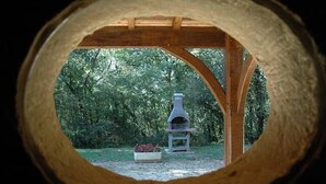 A view through a wooden archway with a stone fireplace in a garden. - COTTAGE *** with pool near Sarlat, Dordogne Périgord Noir (Prats-De-Carlux)