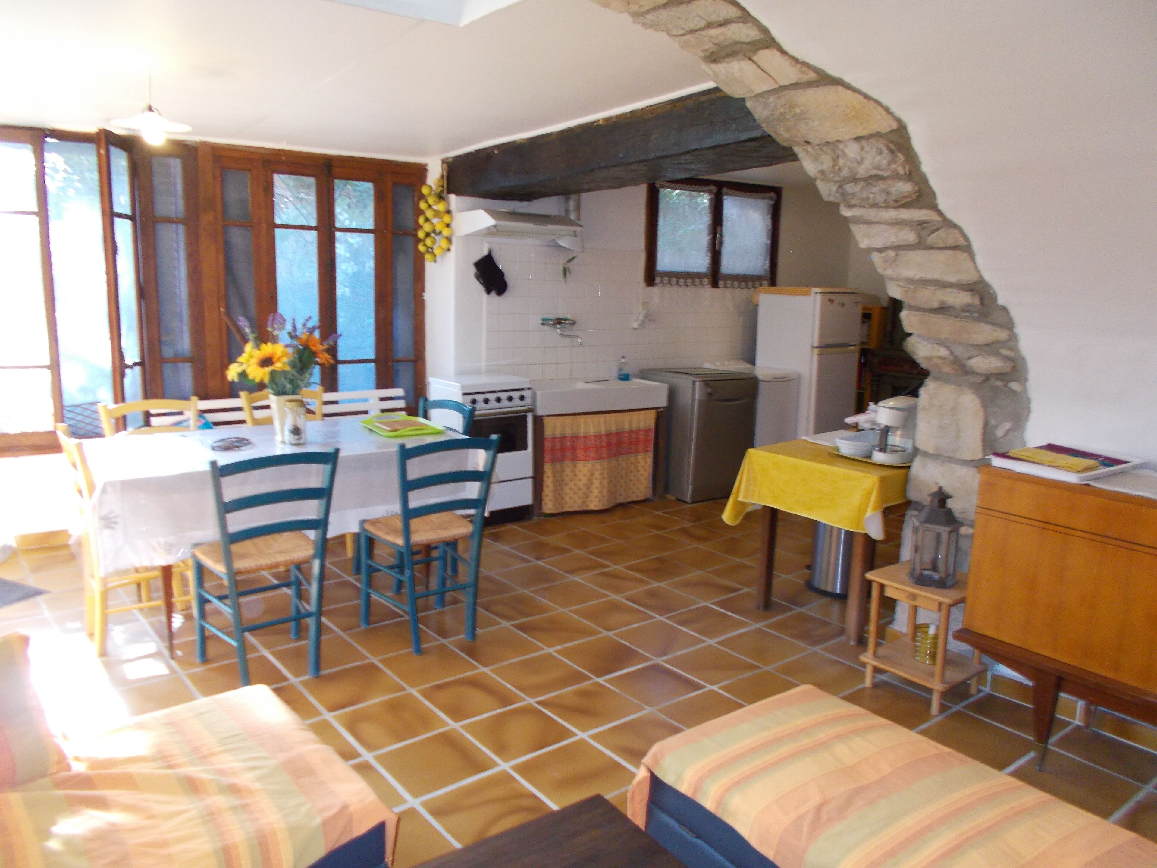Une cuisine avec un coin repas, une arche en pierre et une petite table recouverte d’une nappe jaune.