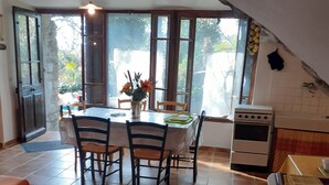 Un coin repas avec une table et des chaises, une cuisine équipée d’une cuisinière et une vue dégagée grâce à de grandes fenêtres.