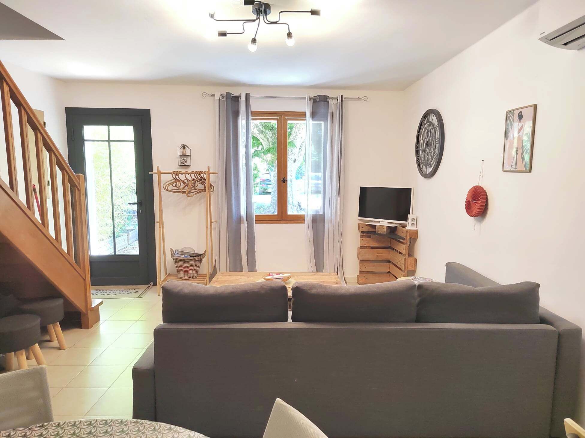 A living room with a sofa, a TV on a wooden stand, a staircase, and a window with curtains.