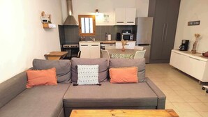 Una sala de estar moderna con un sofá gris, una mesa de centro de madera y una cocina al fondo.