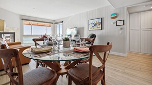 A dining area with a glass table, wooden chairs, and a view of the sea.
