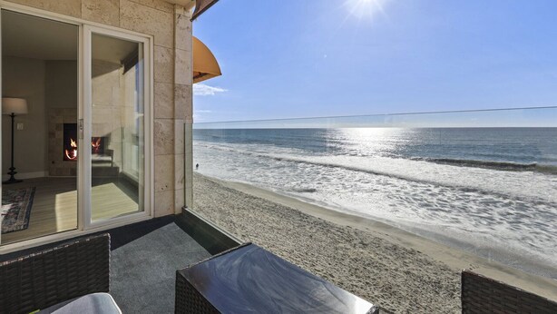 A balcony with a view of the beach and ocean, a fire feature, and outdoor seating.