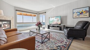 A living room with a fireplace, a large TV, a leather armchair, and a view of the ocean.