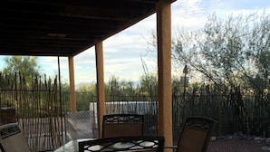 Eine Terrasse im Freien mit Tisch und vier Stühlen, umgeben von einem Zaun und Bäumen.