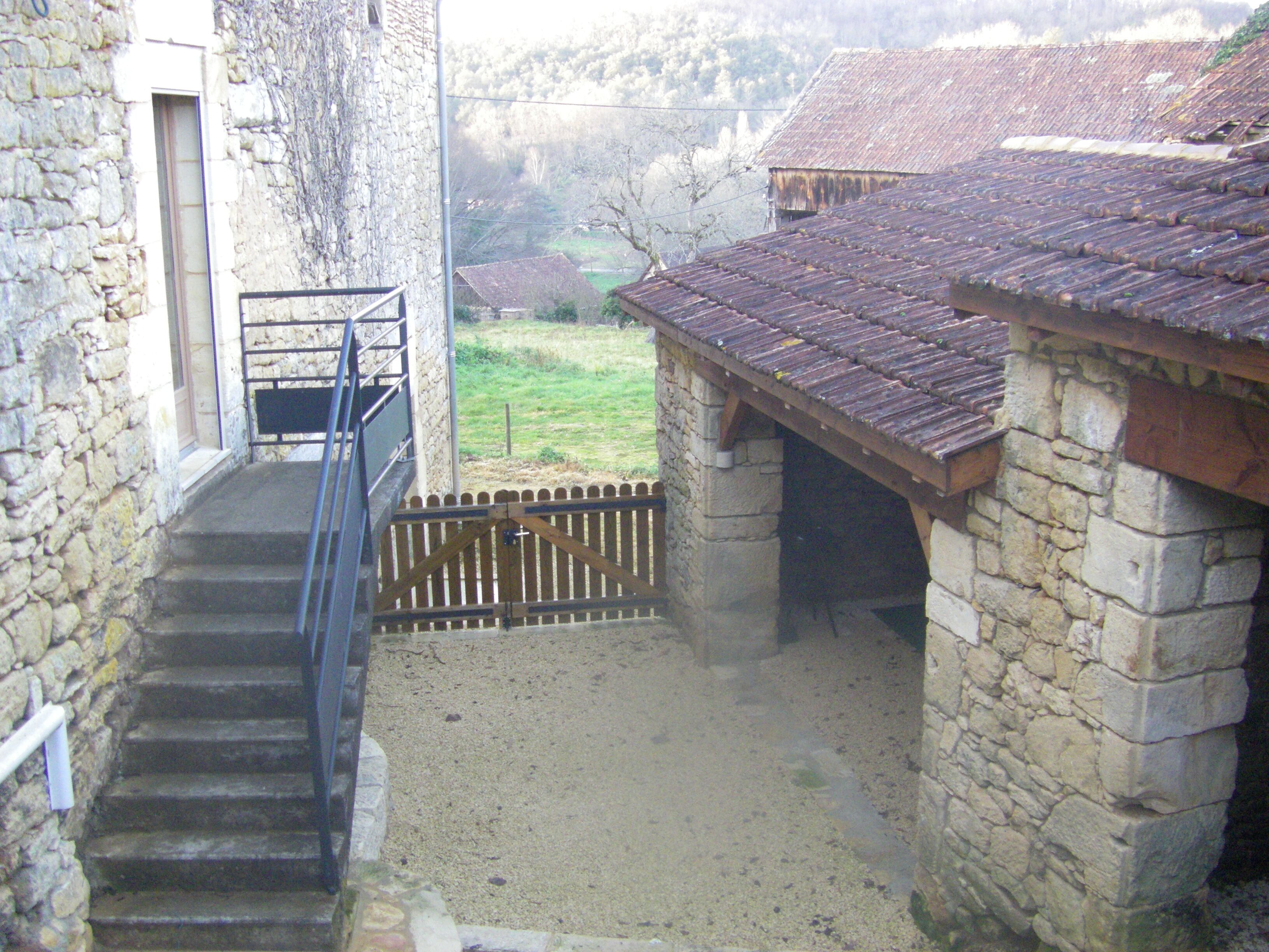 A stone staircase leading to a wooden door, a stone wall, and a view of a rural landscape with houses.
