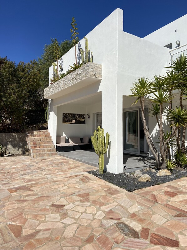 A modern house with a stone-tiled patio, a cactus, and a stone wall.