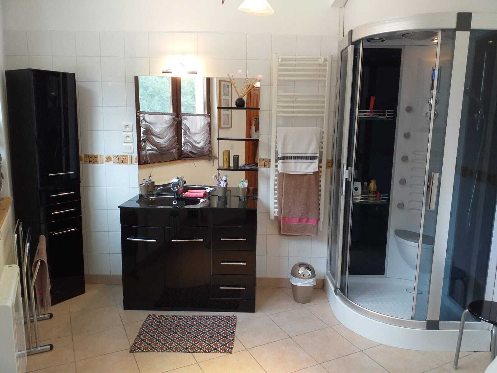 A modern bathroom with a black vanity, a glass shower enclosure, and a white tiled floor.