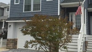 A two-story house with a garage, a small tree in the front yard, and an American flag on the front porch. - Bayfront with dock and fire pit, @ Harris Harbor, Beach  Haven Park, LBI (Long Beach Township)