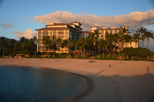 Ein Strandhotel mit mehreren Etagen, Palmen und Strandsonnenschirmen.