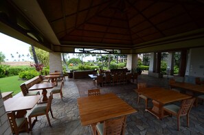 Eine Terrasse im Freien mit Holztischen und -stühlen, einem Steinfußboden und Blick auf einen angelegten Garten.