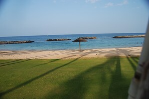 Ein Strand mit einem Reetdachschirm, klarem blauen Wasser und Felsformationen.