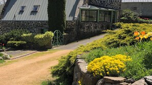 Une maison en pierre avec un toit végétalisé, un mur de pierre orné de fleurs jaunes et un chemin de gravier.