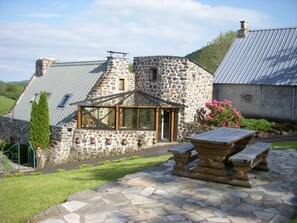 A stone house with a sloped roof, a glass conservatory, and a stone patio with a wooden table. - Auvergne Puy de dôme 1140 m calm and relaxation assured swimming pool  (Saint-Alyre-ès-Montagne)