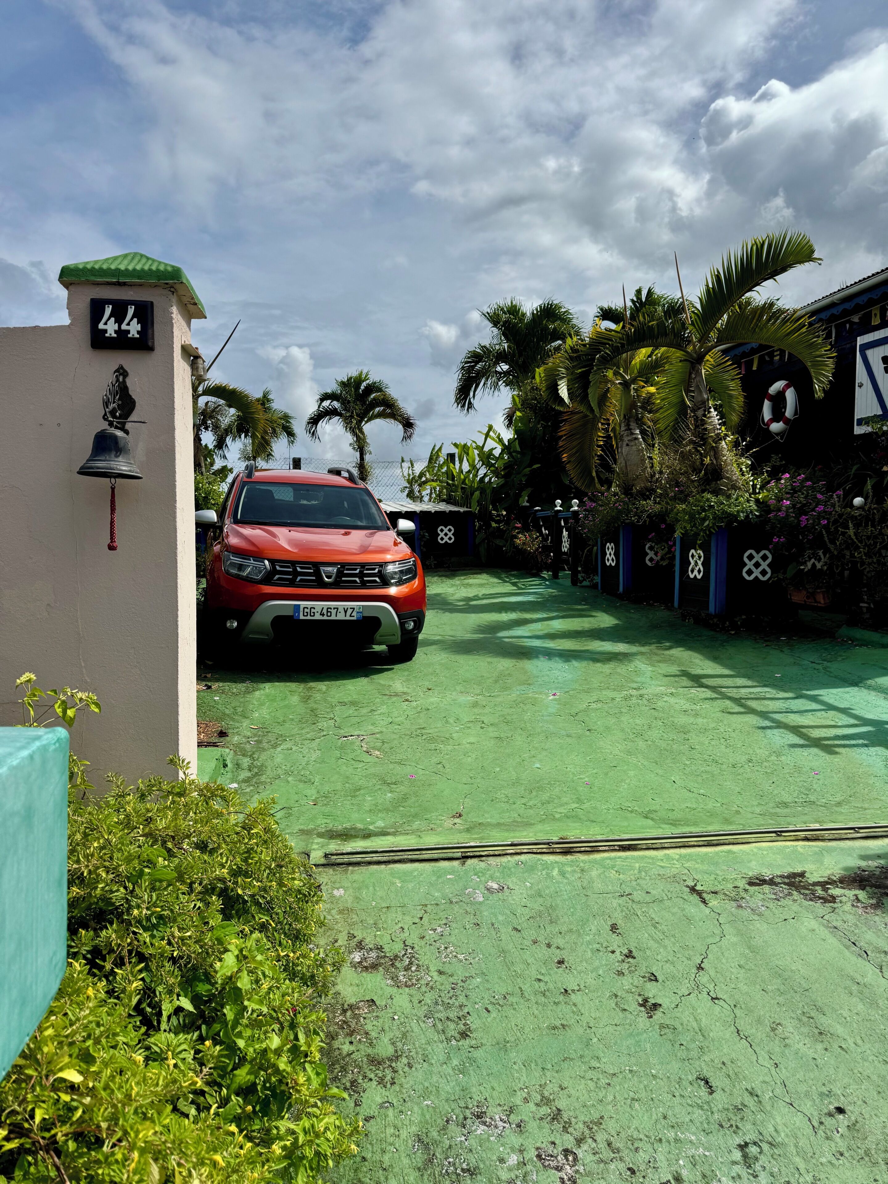 A red car parked in a driveway with a house number 44, a bell, and a lifebuoy on the wall.