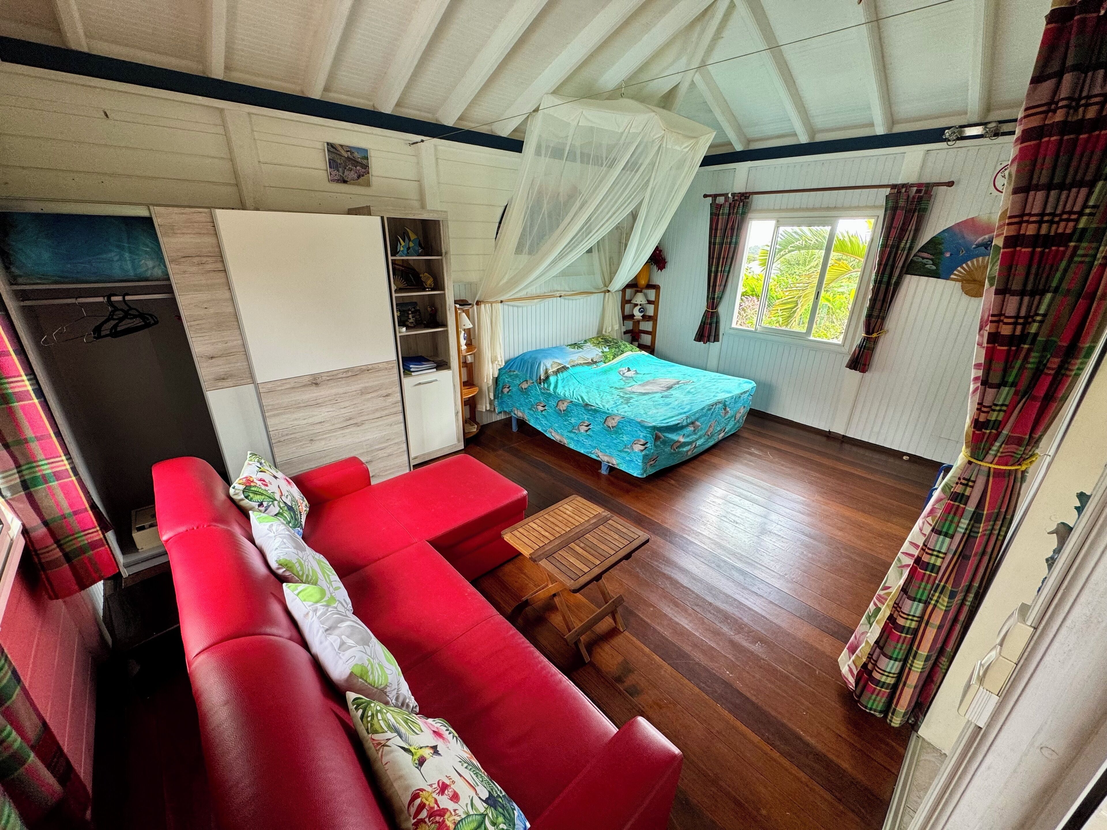 Una habitación pequeña con cama, sofá rojo, una mesita y un armario.