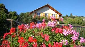 Et hus med balkon, omgivet af en have med røde og lyserøde blomster.