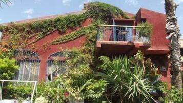 A building with a red facade, a balcony with metal railings, and lush greenery growing on the walls.
