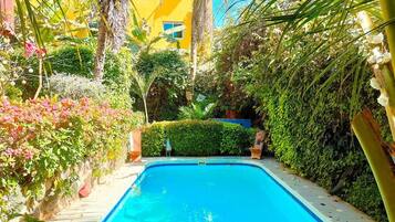 A swimming pool surrounded by lush greenery and a yellow building.